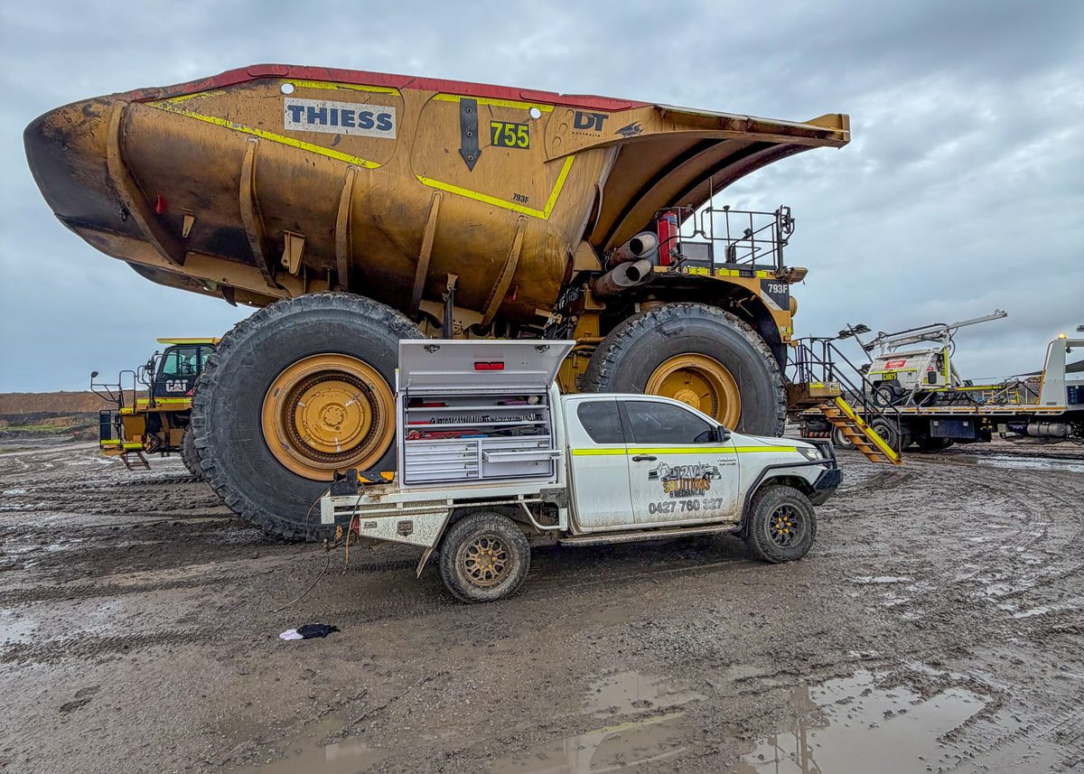 Large dump truck and smaller vehicle on a construction site with a cloudy sky.