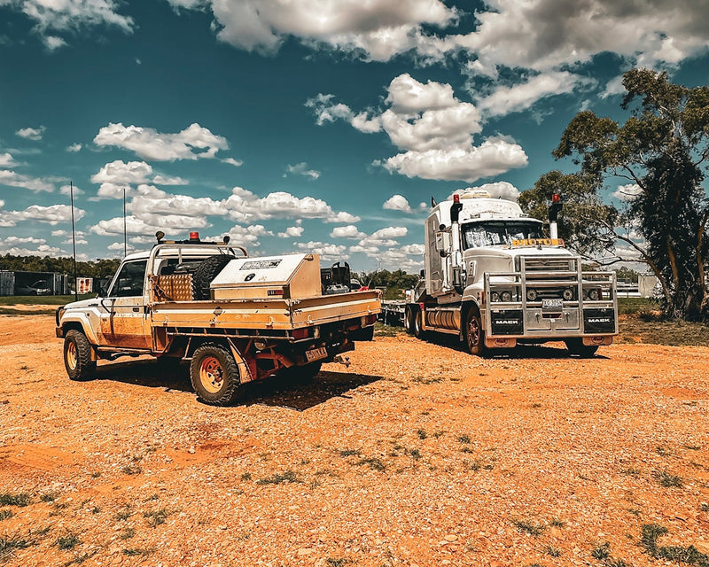Two trucks on a dirt road with a clear sky