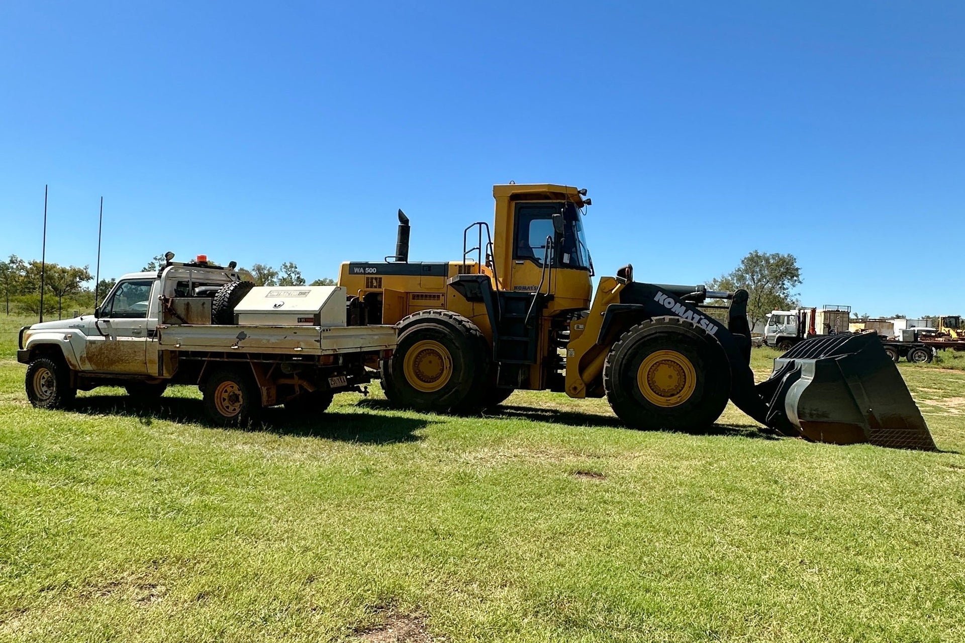 Yellow loader with a truck on a grassy field with a clear blue sky.
