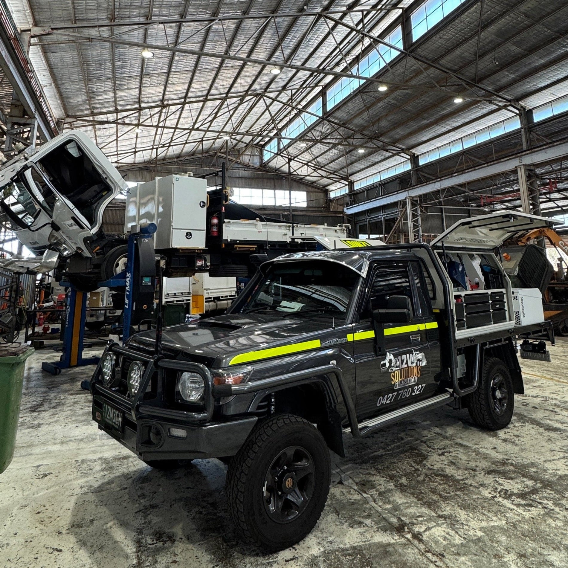 Black utility truck with yellow stripe inside a large industrial building.