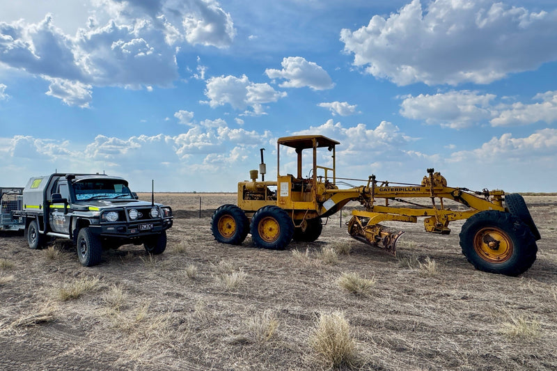 Truck and large piece of construction equipment in a desert landscape with a blue sky.